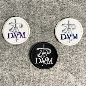 May include: Three round embroidered patches with a snake and staff symbol and the letters "DVM" in the center. One patch is white with silver embroidery, one is white with purple embroidery, and one is black with silver embroidery.
