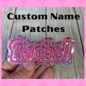 May include: A pink and iridescent custom name patch with the name "Rachel" embroidered in pink.