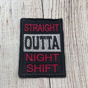 Op de afbeelding: Zwarte geborduurde patch met witte en rode letters die "Straight Outta Night Shift" lezen.
