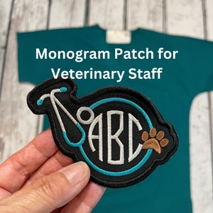 May include: A black and teal embroidered patch with a stethoscope and a circle containing the letters "ABC" and a brown paw print. The text "Monogram Patch for Veterinary Staff" is above the patch.