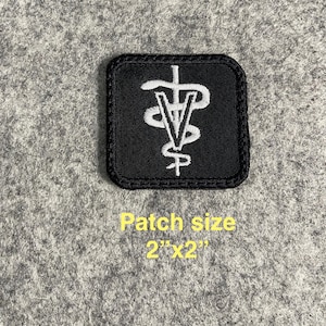 May include: A square black patch with a white veterinary symbol. The patch is 2 inches by 2 inches. The symbol features a staff with a snake wrapped around it, and the letter "V".