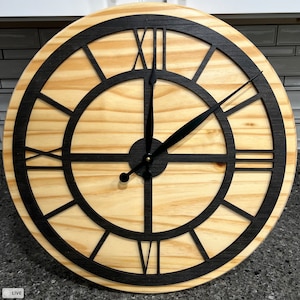 Può includere: Un orologio rotondo in legno con numeri romani neri e lancette nere. Il quadrante dell'orologio è circondato da una cornice nera.