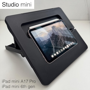 May include: A black tablet stand labeled Studio mini, holding a tablet displaying a mountain landscape and app icons. A white stylus rests in a slot above the screen. The text iPad mini A17 Pro and iPad mini 6th gen is printed at the bottom.