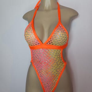 Puede incluir: Un body de malla naranja brillante, rosa y amarillo con pedrería. El body tiene una tira de cuello halter y un escote pronunciado.