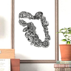 May include: Black and white art print of Florida, filled with intricate patterns and details, framed in a light brown wooden frame. The artwork is displayed on a dark wooden surface, with a potted plant and books in the background.