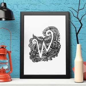 May include: Black framed art print featuring a detailed black and white illustration of the letter "W" within an abstract design. The artwork is displayed on a white surface, with a red lantern and black lamp in the background.