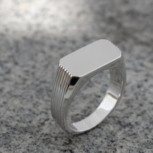 May include: A polished silver signet ring with a rectangular face. The ring has a smooth, reflective surface and a textured band. The ring's design is simple and elegant, suitable for everyday wear.