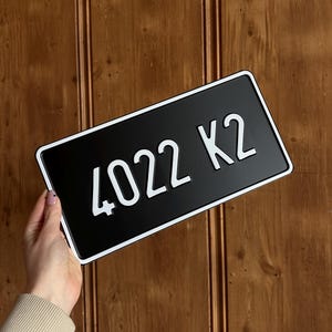 May include: Black license plate with white border and text "4022 K2". The plate is rectangular and has a glossy finish. The background is a wooden surface.