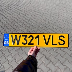 May include: A yellow and black license plate with the text "W321 VLS" and a blue and white European Union flag with the letters "GB" for Great Britain.