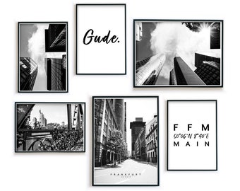 May include: Black and white photo prints of Frankfurt, Germany. The prints feature different views of the city, including skyscrapers, street scenes, and a sign with the city's name and coordinates. The word "Gude" is written in black on a white background on one of the prints.