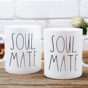 May include: Two white ceramic mugs with black text that reads "Soul Mate".
