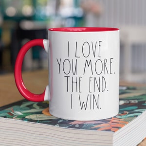 May include: White ceramic mug with a red rim and handle. The mug has black text that reads "I love you more. The end. I win."