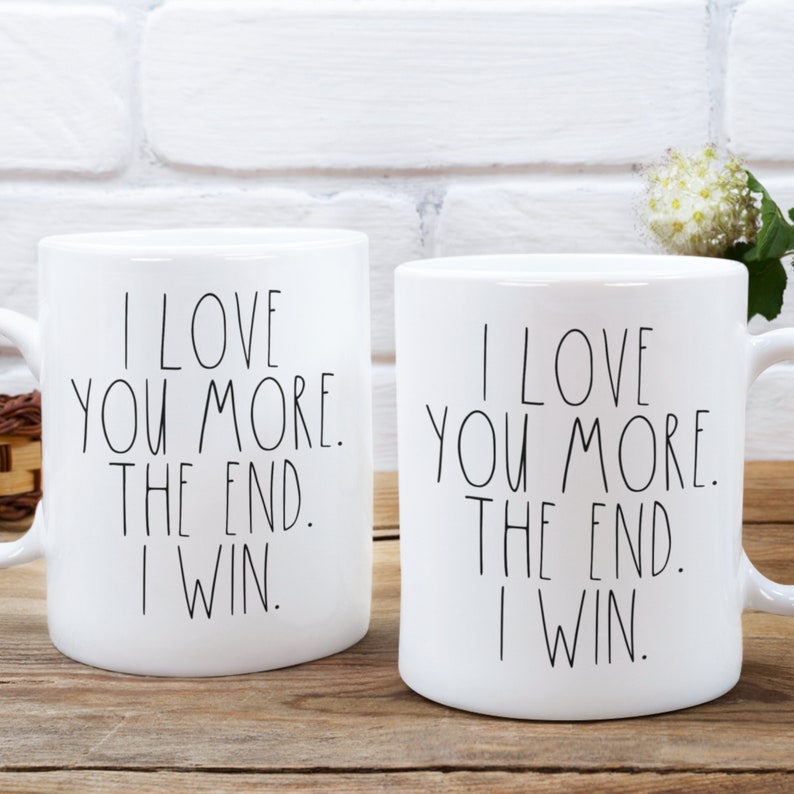 May include: Two white ceramic mugs with black text that reads "I love you more. The end. I win."