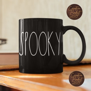 May include: Black ceramic coffee mug with a white "Spooky" design. The mug has a rounded handle.