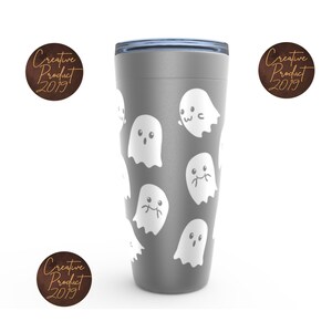 May include: A grey stainless steel travel tumbler with a white ghost pattern. The tumbler has a lid with a blue silicone ring.
