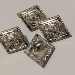 May include: Four silver-toned, diamond-shaped buttons. Each button features a detailed embossed design of a floral or heraldic motif within a square frame. One button is stamped "MADE IN ENGLAND".