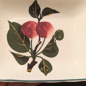 Peut inclure: Un plat carré en céramique blanche avec une bordure verte. Le plat présente un motif peint à la main d'une branche de cerisier avec deux cerises rouges et des feuilles vertes. Les feuilles ont des accents dorés.