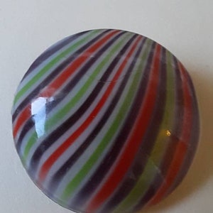 Op de afbeelding: Een ronde, kleurrijke glazen knikker met een wervelpatroon. De knikker heeft afwisselende strepen van rood, groen, paars en wit. De knikker heeft een diameter van ongeveer 3,8 cm.