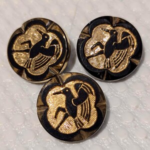 May include: Three black and gold buttons with a stylized bird design. The buttons are round and have a raised design.