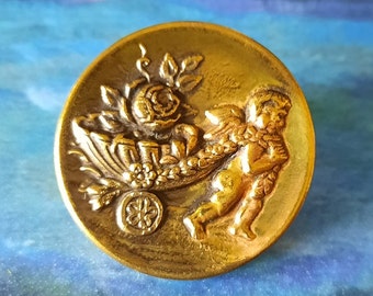 Button scarce of cherub pulling a shell cart. 1.2 inch diameter.