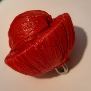 Pode incluir: Um chapéu vermelho tecido com um anel de prata preso na parte inferior.