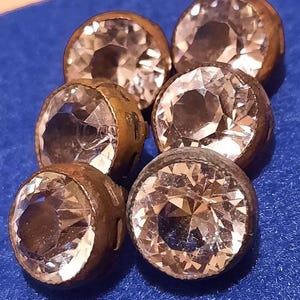 Puede incluir: Seis botones antiguos de vidrio con acabado de cobre. Los botones son redondos y tienen un diseño facetado en relieve. Los botones son de varios tonos de marrón y beige.