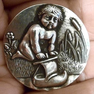 Button cherub by the river with a boat in silver . Large 3cm diameter.