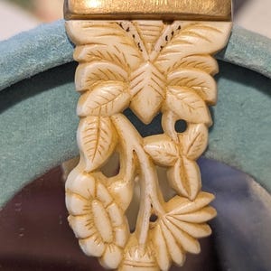 Peut inclure: Fermoir floral sculpté de couleur ivoire avec un dessus en métal doré. Le fermoir présente des feuilles, des fleurs et un motif de papillon détaillés. Le fermoir est probablement destiné à un sac à main ou à un autre accessoire.