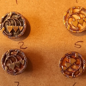 Puede incluir: Cuatro botones antiguos con un diseño floral y un acabado dorado. Los botones tienen un fondo blanco con detalles dorados y tres hojas doradas.