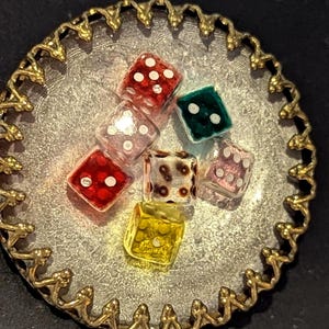 May include: A collection of colorful dice in various colors, including red, green, and yellow, are arranged on a silver-colored, scalloped-edge tray with a gold-colored trim. The dice have white dots.