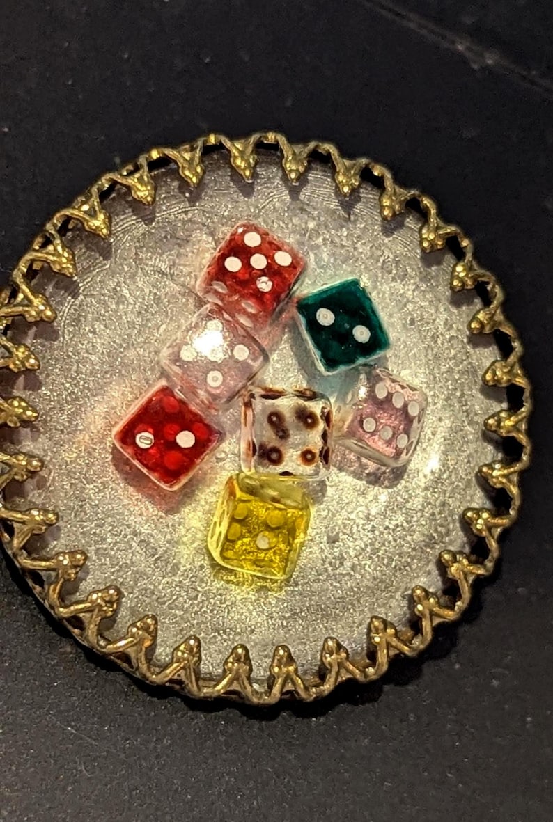 May include: A collection of colorful dice in various colors, including red, green, and yellow, are arranged on a silver-colored, scalloped-edge tray with a gold-colored trim. The dice have white dots.
