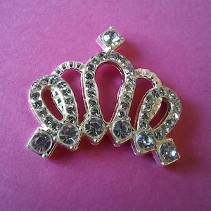 May include: A silver crown with a pointed top and five points, each decorated with clear rhinestones.