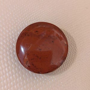 May include: A round, polished stone with a deep reddish-brown color and subtle dark speckles. The stone has a smooth, glossy surface and appears to be a natural gemstone. The stone is a decorative item.