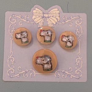 May include: Four round buttons with a tan background, each featuring a hand-painted dog portrait. The dog has gray fur and a green collar. The buttons are arranged on a light blue card with a decorative bow and floral border.