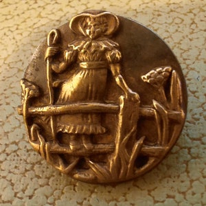 Knoop Kate Greenaway. Gouden voorkant op tinnen achterkant. Doorsnee 1,8 cm.