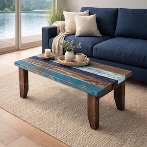 May include: A rectangular wooden coffee table with a distressed finish. The tabletop features alternating stripes of blue, brown, and natural wood tones. The legs are a dark brown color. The table is placed on a beige rug.