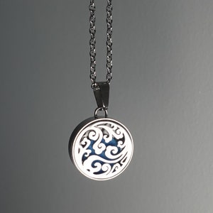 Puede incluir: Un collar de plata con un colgante redondo que presenta un diseño delicado e intrincado de líneas y formas en espiral. El colgante tiene un centro azul.