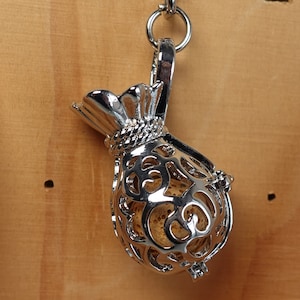 May include: A silver charm in the shape of a money bag with an intricate design. The bag is open at the top and has a rope-like detail around the opening.