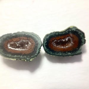 May include: Two halves of a geode, showcasing a dark green exterior, a brown middle layer, and a sparkling crystal center. The cut reveals the natural beauty of the stone, with a focus on the contrasting colors and textures.