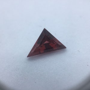 Puede incluir: Una piedra preciosa triangular facetada de color rojo oscuro.
