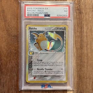 May include: A graded Pokemon trading card featuring Raichu, a yellow electric-type Pokemon with a lightning bolt tail. The card is from the 2006 Holon Phantoms set and is graded NM (Near Mint) 7 by PSA.