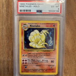 Puede incluir: Una carta de Pokémon holográfica que presenta a Ninetales, un Pokémon zorro con una cola naranja ardiente y un fondo azul. La carta está calificada como EX-MT 6 por PSA y tiene el número 12. El texto de la carta dice "Muy inteligente y muy vengativo. Agarrar una de sus muchas colas podría resultar en una maldición de 1.000 años. NV. 32 #38".
