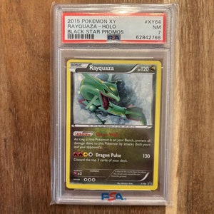 May include: A holographic Pokemon trading card featuring Rayquaza, a green dragon-like creature with a blue and white background. The card is from the 2015 Pokemon XY Black Star Promos set and is graded NM 7 by PSA.