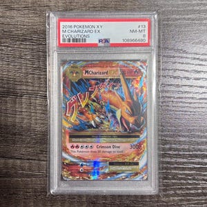 May include: A graded Pokémon card featuring a Mega Charizard EX from the 2016 Evolutions set. The card is encased in a protective holder and displays vibrant artwork of Charizard. The card is graded NM-MT 8.