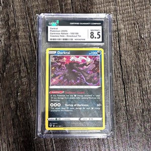 May include: A graded Darkrai Pokémon card from the Darkness Ablaze set, encased in a protective holder. The card is graded 8.5 by the Certified Guaranty Company. The card features a Darkrai illustration with the text "Darkrai" and "-120".