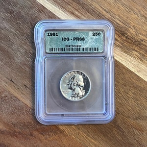 May include: A 1961 25c US quarter coin graded PR68 by ICG in a plastic slab with the grading label visible. The label includes the year, grade, and certification number 2087000202.