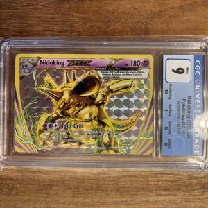 Puede incluir: Una carta de Pokémon Nidoking BREAK del set Evoluciones, clasificada y protegida en una funda. La carta ha obtenido una calificación CGC Universal Grade de 9. La carta es de color dorado y amarillo con una ilustración en blanco y negro de Nidoking BREAK.