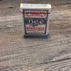 Puede incluir: Una baraja de cartas Bee en una caja azul y blanca. La caja dice "No. 07 Club Special" y "Bee" con una ilustraci&oacute;n de abeja. La caja tambi&eacute;n dice "Pinochle Playing Cards" y "The N.Y. Consolidated Card Co."