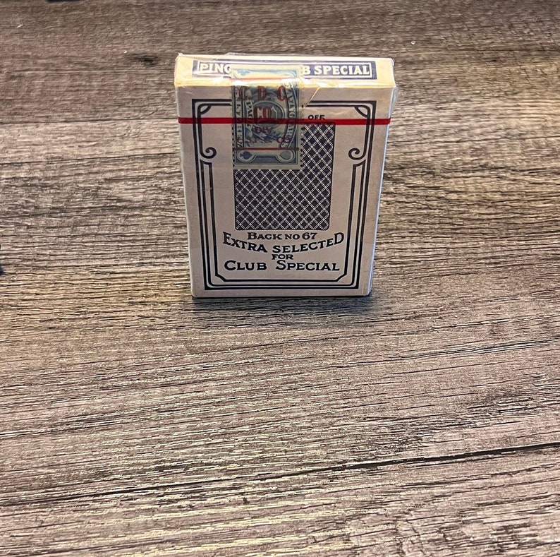 Puede incluir: Una baraja de cartas en una caja blanca con detalles azules y rojos. La caja dice "Back No 67 Extra Selected for Club Special".