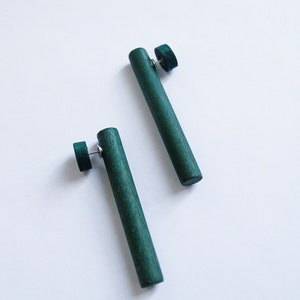 May include: A pair of dark green wooden earrings. Each earring is a long, thin cylinder with a small round disc at the top.